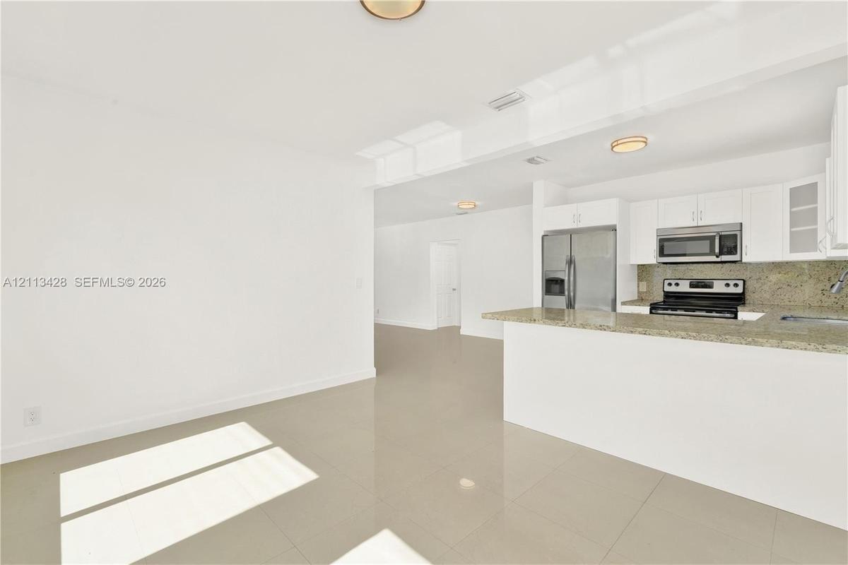 Kitchen featuring white cabinetry, stone-surface countertops, stone-finish backsplash, and stainless steel appliances, complemented by large-format ti