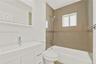 Bathroom featuring a white vanity with an integrated basin, a large wall-mounted mirror, a bathtub with a tiled shower surround, and a chrome hand-hel