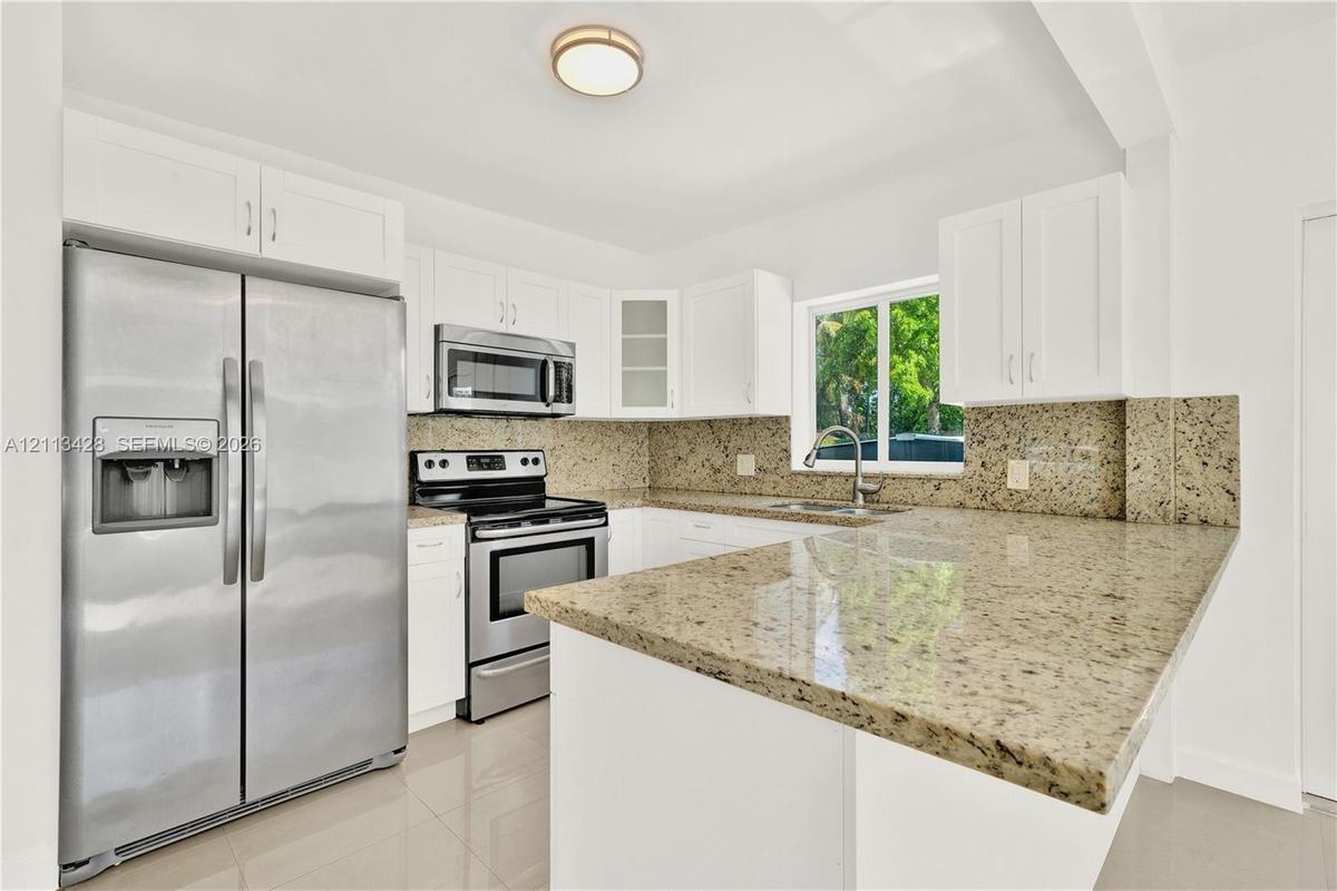 Kitchen featuring white shaker-style cabinetry, stone countertops, stainless steel appliances, and a dual-basin undermount sink