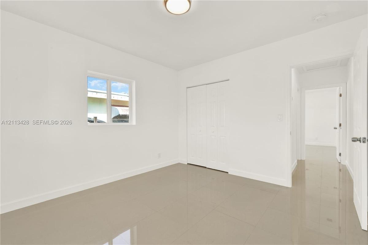 Neutral-toned tile flooring, white interior walls, sliding door closet, single-pane window, and flush-mount ceiling lighting