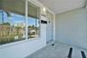 Covered entryway featuring a painted brick accent wall, large picture window, stone-finish tile flooring, and wall-mounted exterior lighting