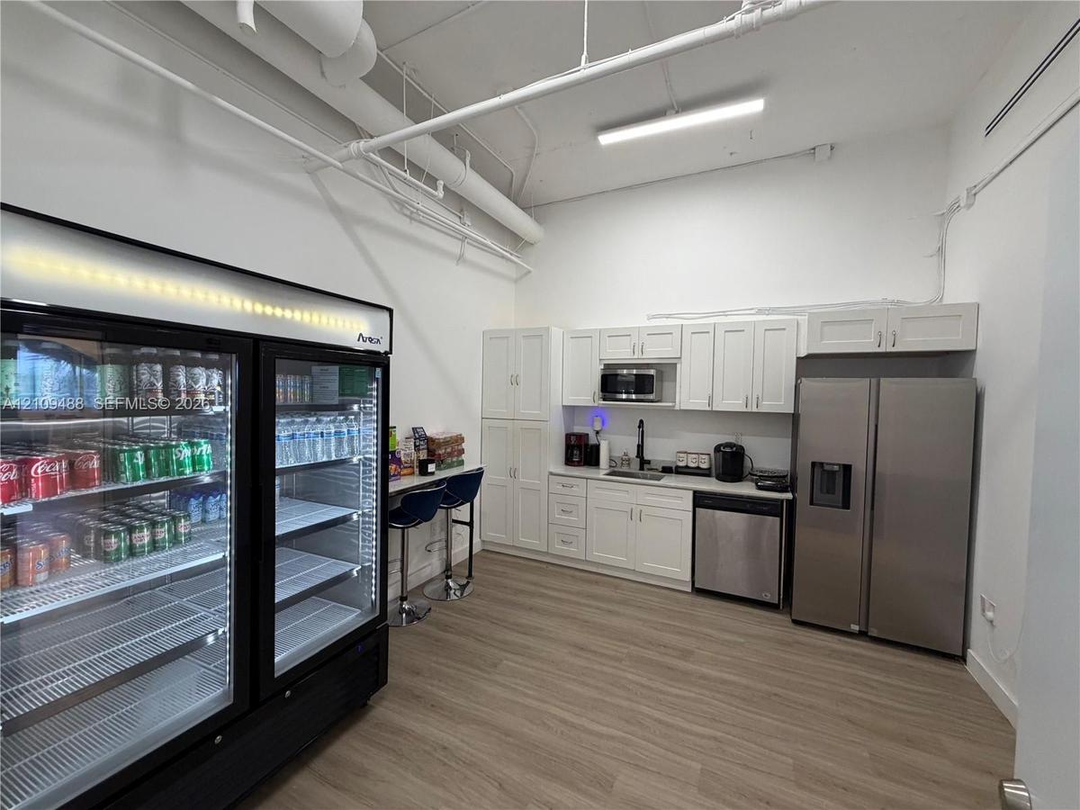 Kitchenette featuring white cabinetry, stainless steel appliances, a built-in microwave, wood-finish flooring, and high ceilings with exposed mechanic