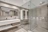 Floating double vanity with integrated sinks, large wall-mounted mirror, glass-enclosed walk-in shower with overhead rainfall fixture, and floor-to-ce