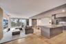 Open-concept interior featuring light wood-finish flooring, a central kitchen island with a stone-surface countertop, built-in recessed cabinetry, and