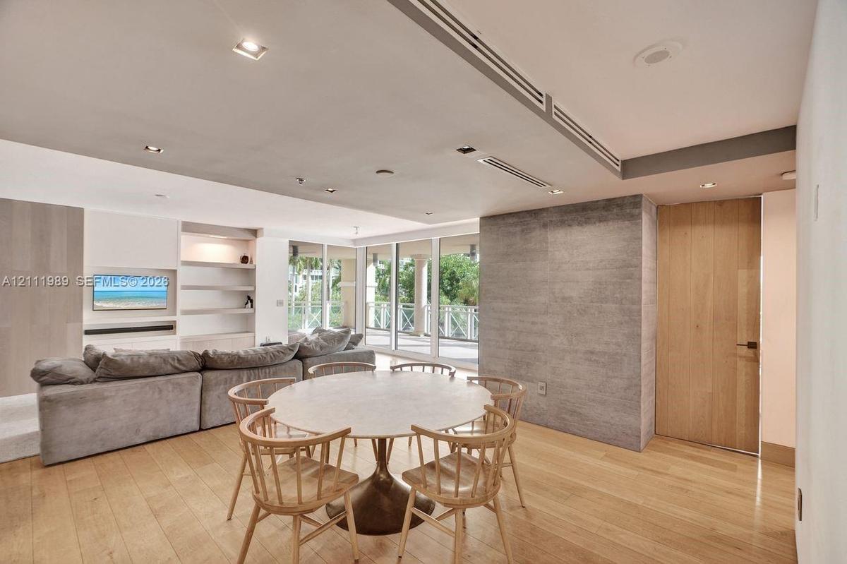 Open-concept area featuring wood-finish flooring, recessed lighting, built-in shelving, a textured stone-finish accent wall, and floor-to-ceiling glas