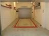 Automated vehicle elevator featuring a metal platform, industrial rolling steel door, surface-mounted wall tracks, and recessed ceiling lighting