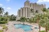 Multi-story residential building exterior featuring a swimming pool, integrated spa, paved terrace, and mature palm trees