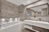 Modern floating dual-vanity with integrated sinks, floor-to-ceiling stone wall tiling, built-in soaking tub, and wall-mounted faucets