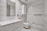 Floating vanity with a white countertop and integrated sink, wall-mounted toilet, floor-to-ceiling stone-style wall tile, frameless mirror, and wall-m