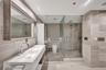 Floating dual-sink vanity with a solid-surface countertop, full-width mirror with wood-finish frame, frameless glass-enclosed shower, and stone-tiled 