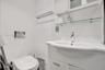 Wall-mounted toilet with chrome flush plate, white vanity cabinet, integrated porcelain sink with single-lever faucet, and glass shelving