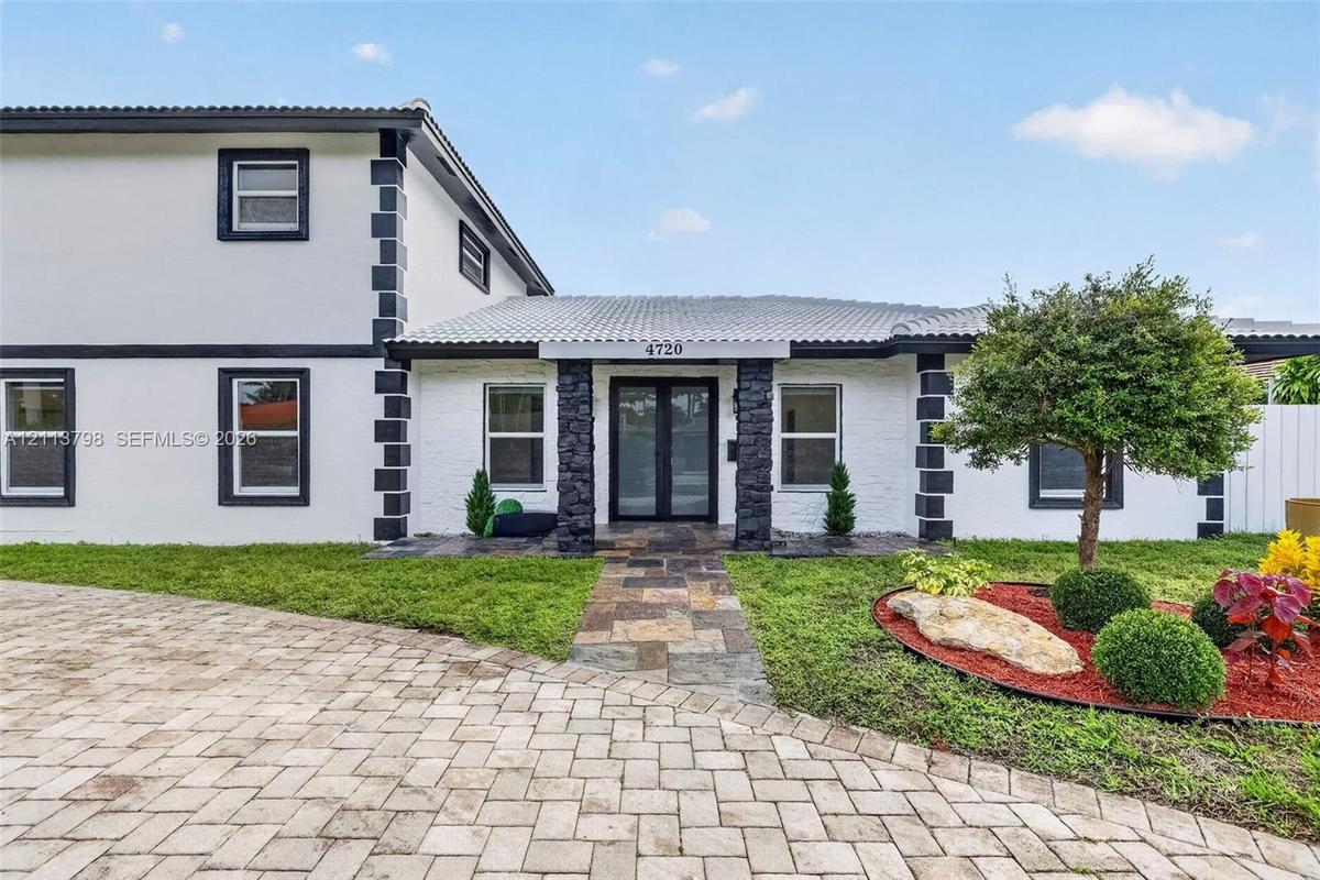 Two-story exterior featuring a white-painted brick facade with dark contrast trim, stone-clad porch columns, a multi-colored stone paver walkway, and 