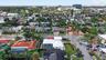 Aerial perspective featuring a white-roofed residence with a screen-enclosed pool, perimeter fencing, and established palm trees in a residential neig