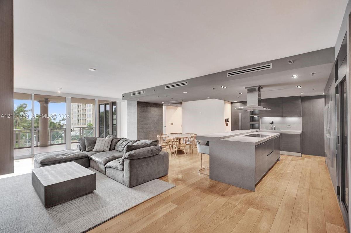 Open-concept kitchen featuring an expansive central island, modern cabinetry, built-in cooktop with stainless steel vent hood, and wood-finish floorin