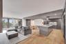 Open-concept kitchen featuring an expansive central island, modern cabinetry, built-in cooktop with stainless steel vent hood, and wood-finish floorin