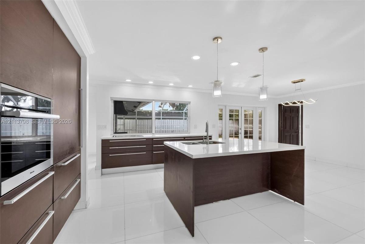 Kitchen featuring flat-panel cabinetry, a central island with a solid-surface countertop, recessed ceiling lighting, pendant light fixtures, and polis