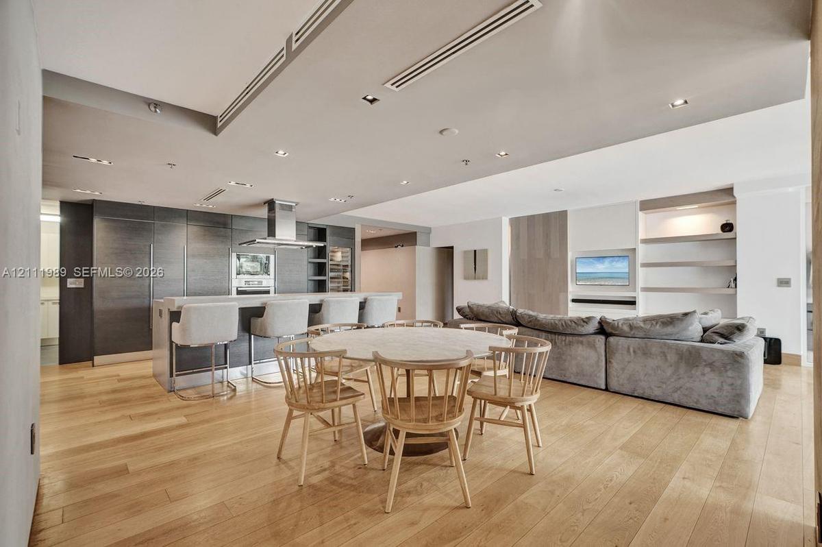 Open concept interior featuring wide-plank wood-finish flooring, custom dark-toned cabinetry, a stainless steel range hood, recessed ceiling lighting,