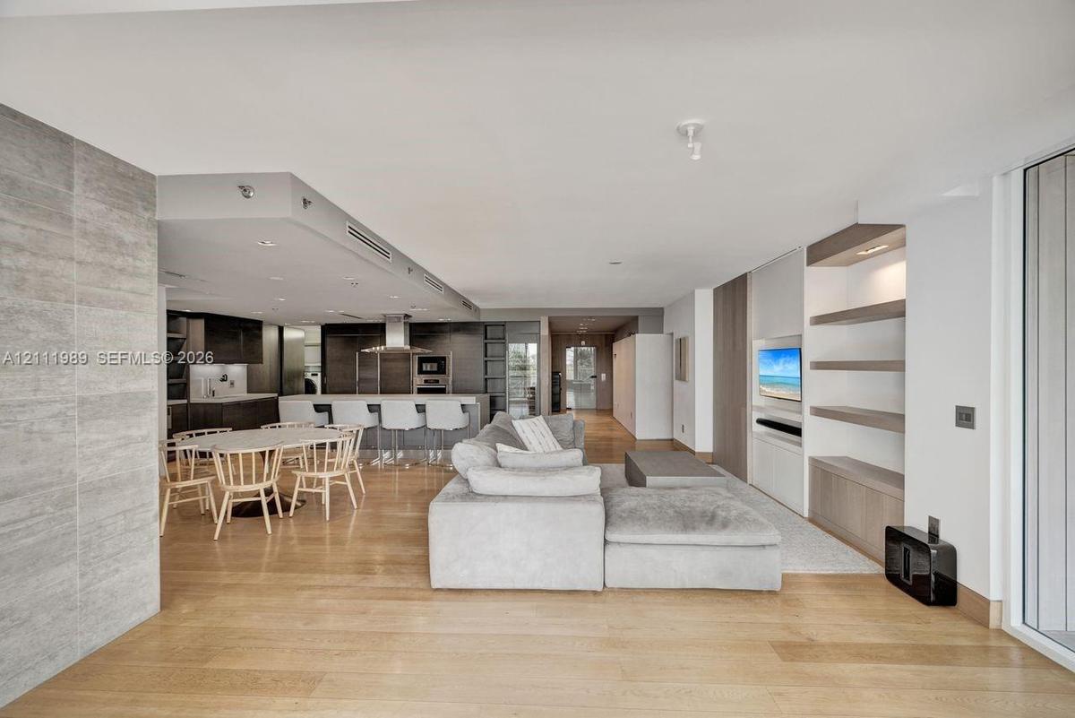 Open-concept interior featuring light wood-finish flooring, a kitchen with a stone-top island, custom cabinetry, and built-in shelving with integrated