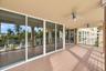 Covered outdoor balcony featuring wood-finish flooring, full-height sliding glass doors, decorative support columns, and ceiling-mounted fans