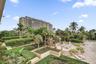 Extensive stone-paved terrace featuring multi-level landscaping, mature palm trees, tiered stone staircases, and a built-in outdoor service bar