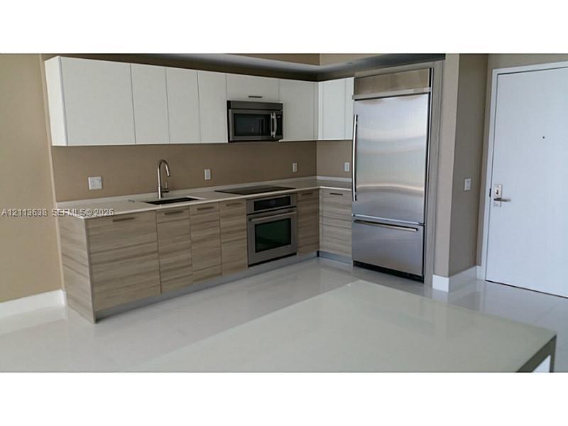 Kitchen featuring two-tone cabinetry with wood-grain finish lower cabinets and matte white upper cabinets, stainless steel appliances, integrated refr