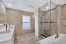 Bathroom featuring natural stone wall and floor tiling, double-basin vanity with solid-surface countertop, glass-enclosed walk-in shower with rainfall