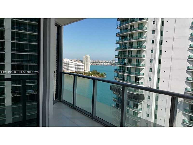 Covered balcony featuring glass pane railings, tile flooring, and water scenery