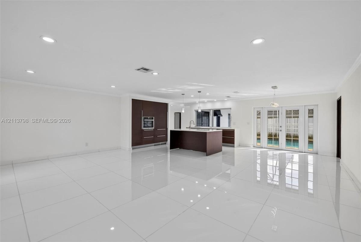 Open-concept kitchen featuring dark wood-finish cabinetry, a central island, recessed lighting, and white tile flooring throughout, accented by French