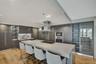Kitchen featuring dark wood-finish cabinetry, a waterfall-edge center island with an integrated cooktop, a stainless steel chimney-style range hood, b