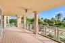 Covered balcony featuring wood-finish flooring, structural stone-finish columns, white cross-patterned railings, and ceiling-mounted fans