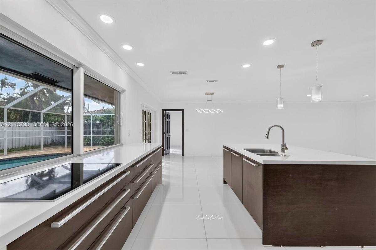 Kitchen featuring dark wood-finish cabinetry, solid-surface countertops, a center island with an undermount sink, porcelain tile flooring, and recesse