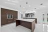 Kitchen featuring dark wood-finish cabinetry, solid-surface countertops, a center island with a built-in sink, stainless steel wall oven, and polished