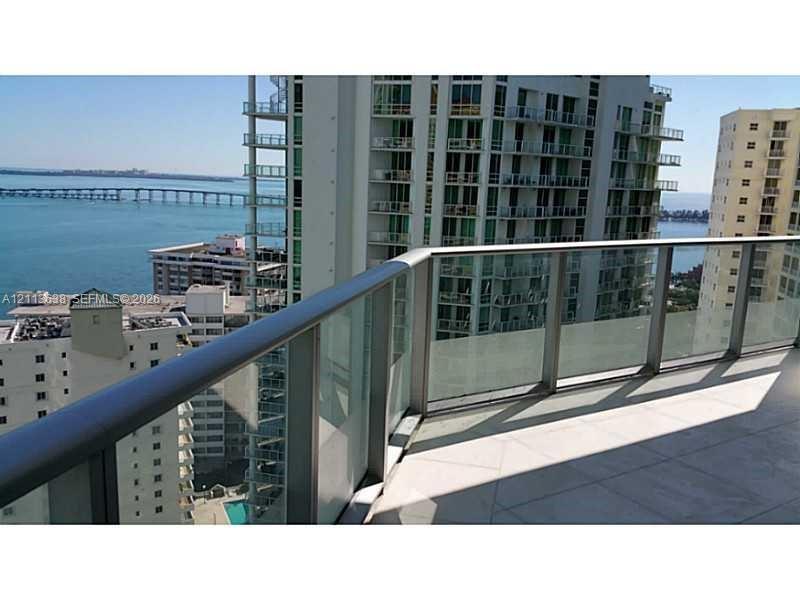 Private balcony featuring large-format tile flooring and a glass panel railing with a metal handrail