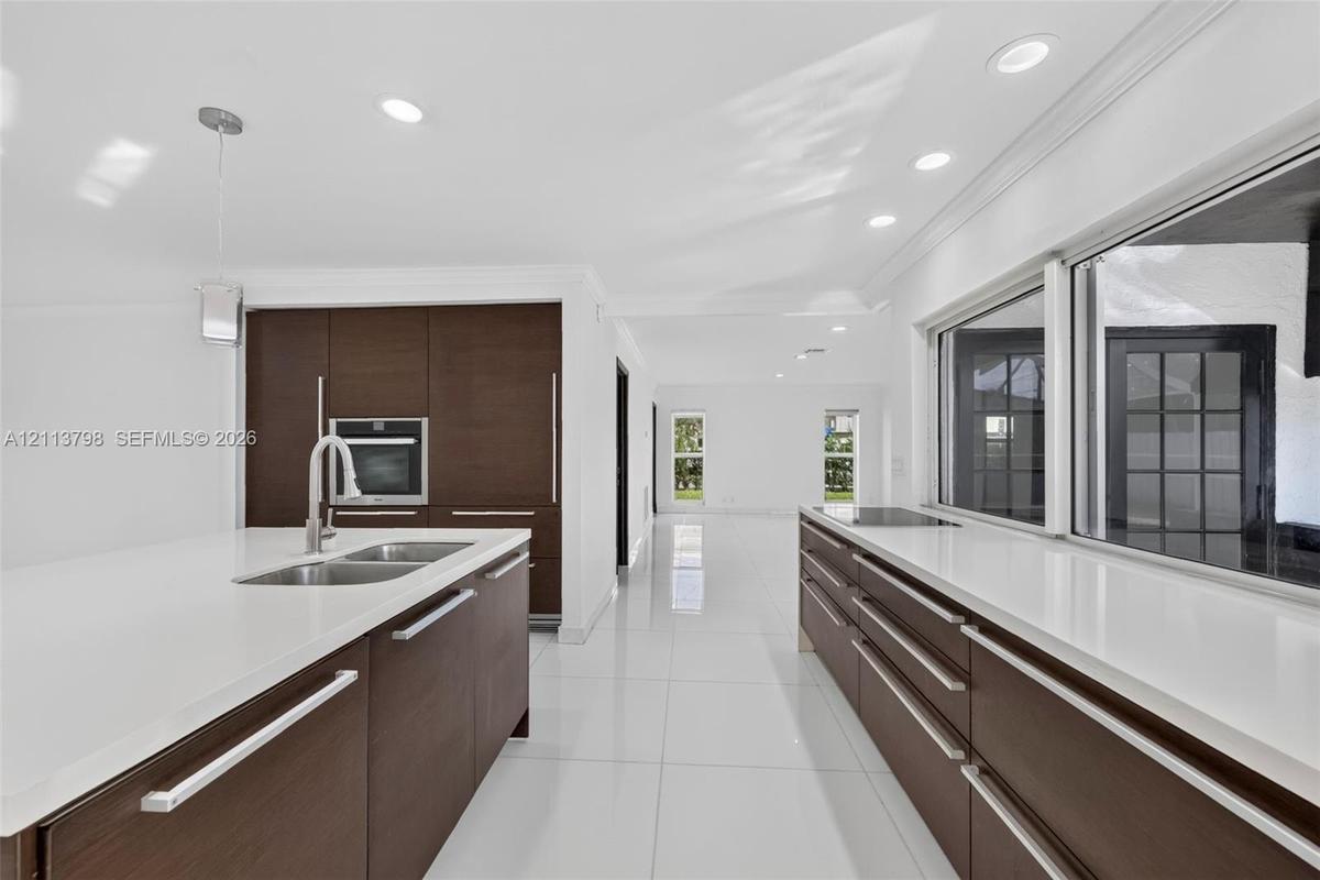 Kitchen featuring dark wood-finish cabinetry, solid-surface countertops, integrated wall oven, stainless steel dual-basin sink with pull-down faucet, 