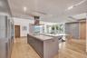 Chef’s kitchen featuring an expansive center island with stone countertop, stainless steel range hood, built-in cabinetry with integrated appliances, 