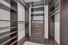 Custom walk-in storage system featuring dark wood-finish cabinetry, built-in shelving, integrated hanging rods, and a centralized unit with four drawe