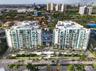 Aerial view of a multi-story residential complex featuring private balconies, central outdoor swimming pool, paved entryway, and manicured landscaping