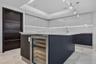 Kitchen featuring high-gloss cabinetry, a central island with a built-in wine refrigerator, stone countertops, recessed tray ceiling lighting, and til