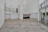 Open-concept interior featuring double-height ceilings, stone-finish tile flooring, a glass-panel mezzanine railing, multi-light pendant chandelier, a