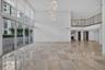 Expansive interior space featuring double-height ceilings, floor-to-ceiling windows, polished stone flooring, a multi-pendant light fixture, and a mez