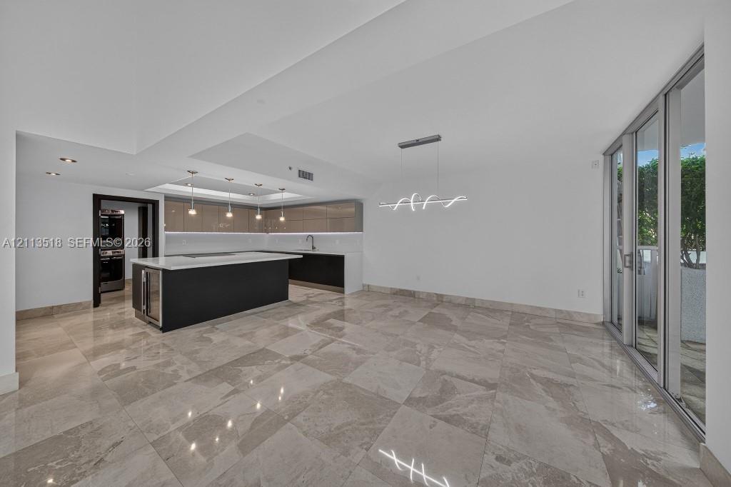 Open-concept area featuring oversized neutral-toned tile flooring, sleek flat-panel cabinetry, a central kitchen island with a stone-finish countertop