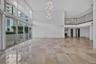 Double-height ceilings, floor-to-ceiling glass wall, polished stone flooring, multi-tiered pendant light fixture, and second-level mezzanine with glas