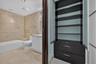 Built-in cabinetry featuring dark wood-finish shelving and drawers with frosted glass doors, complemented by a bathroom finished with stone-tile wall 