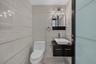 Bathroom featuring floor-to-ceiling large-format tile, wall-mounted dark wood vanity with a white vessel sink, multi-bulb wall-mounted lighting, and a