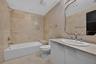 Full-height natural stone wall tiling, white vanity with an integrated countertop, oval undermount sink, decorative wall mirror, and built-in tub surr