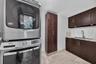 Laundry area featuring dark wood-finish cabinetry, a tall pantry unit, a stainless steel undermount sink with a gooseneck faucet, light-toned stone-fi