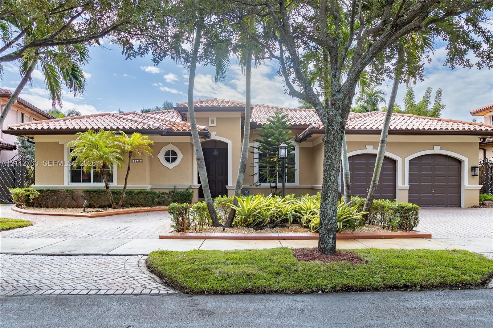 Stucco exterior featuring a clay tile roof, arched double-car garage, paved driveway, and mature landscaping