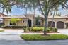 Stucco exterior featuring a clay tile roof, arched double-car garage, paved driveway, and mature landscaping