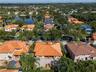 Aerial view featuring a terra cotta tiled roof, paved driveway, and mature palm trees within a residential landscape