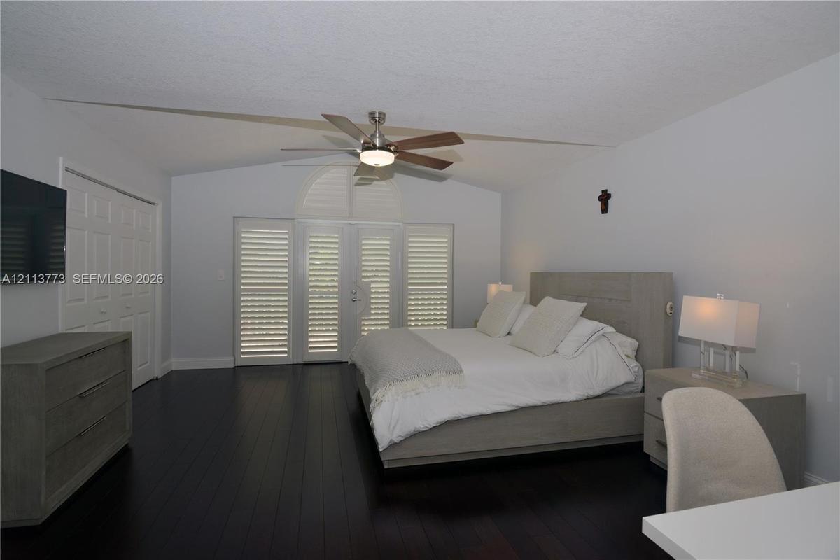 Vaulted ceilings with a central ceiling fan, dark wood-finish flooring, and white louvered plantation shutters on the double doors and windows